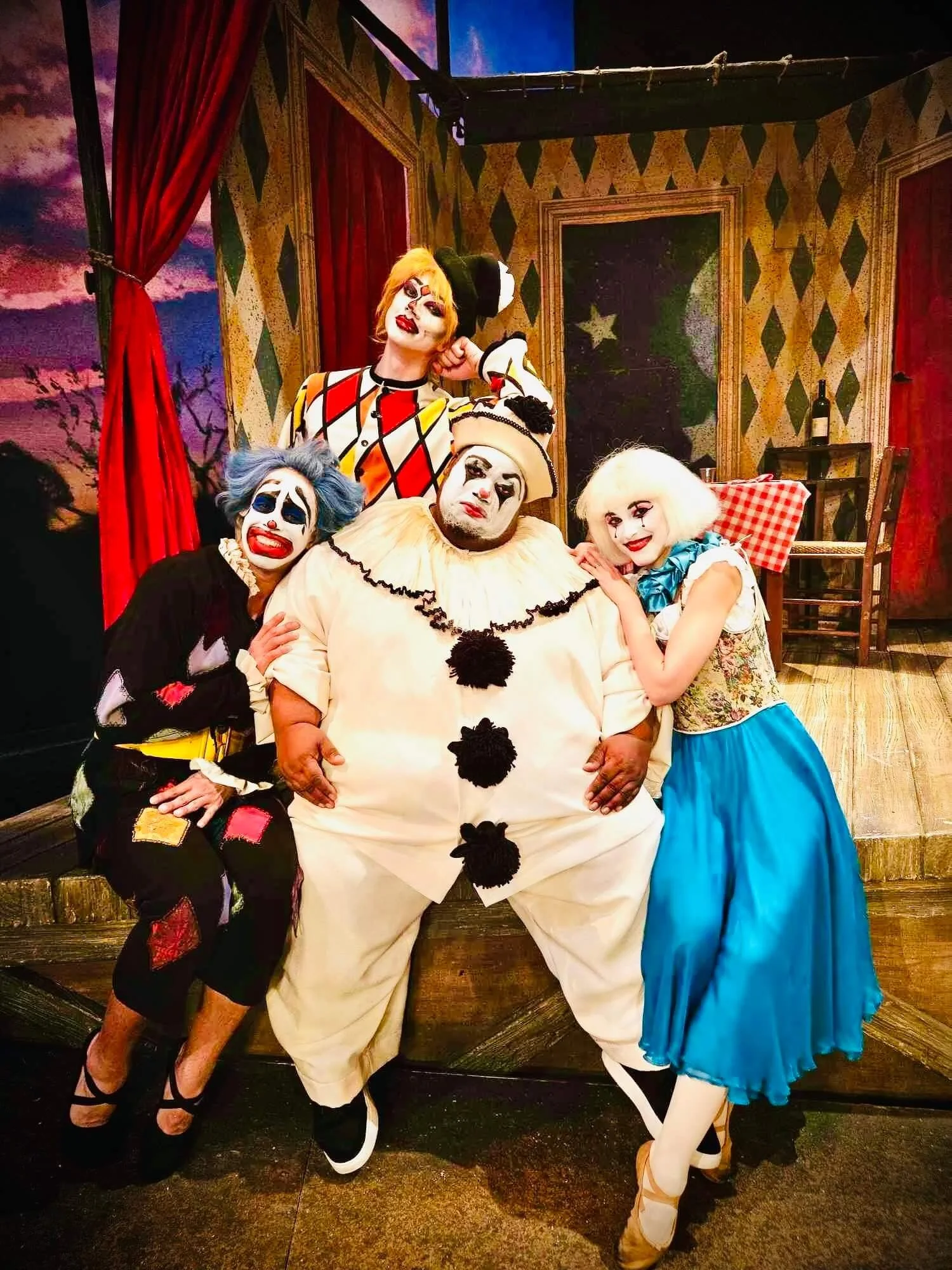 Ballet dancer Emily Ricca with Pagliacci cast in full clown and Commedia dell'arte costumes posing on stage set with harlequin backdrop and red curtains