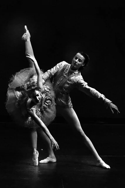 Black and white photo of ballet dancer Emily Ricca in a tutu performing a dramatic pas de deux with male partner, both in ornate costumes under stage lighting