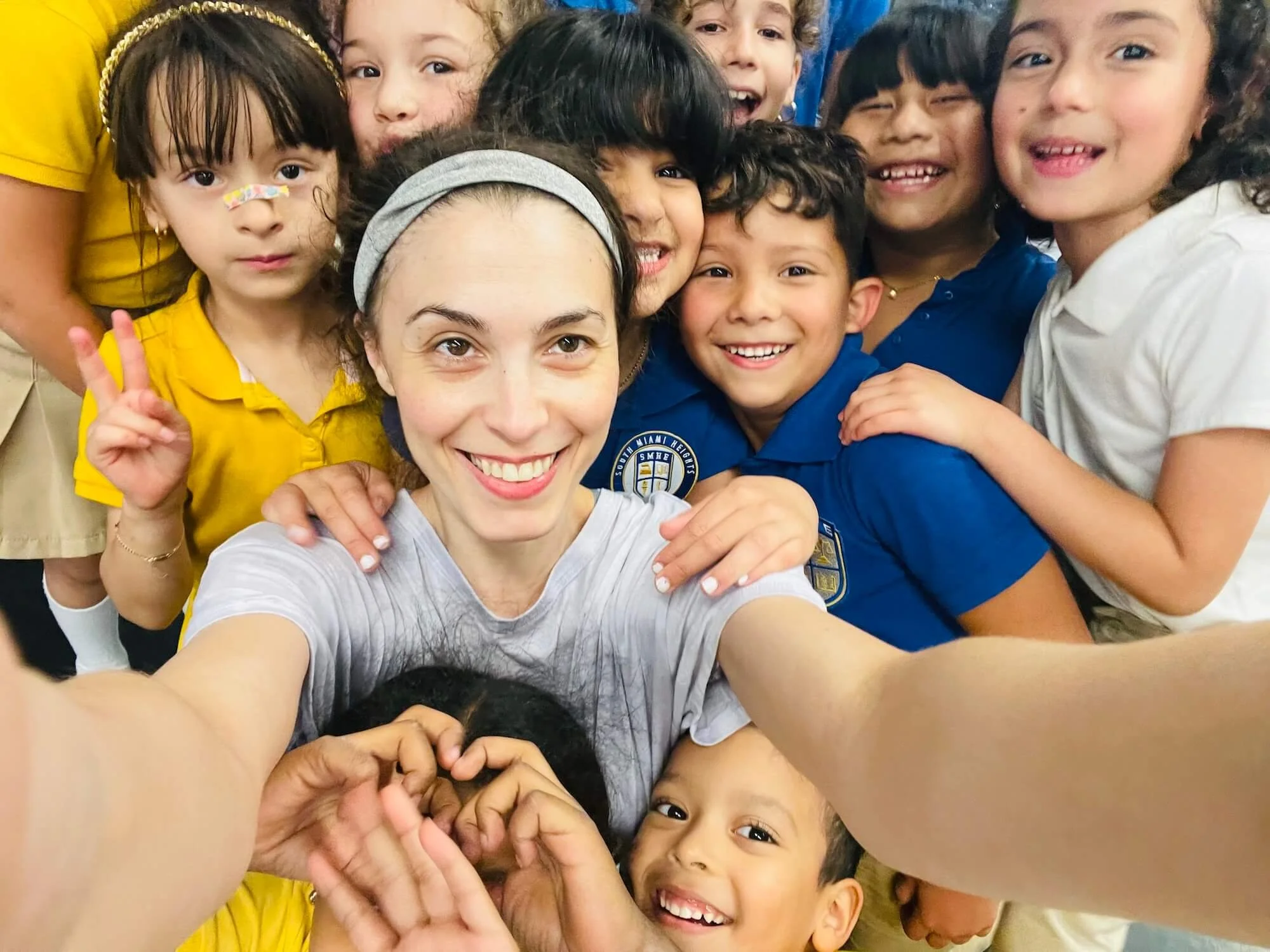 Ballet teacher Emily Ricca smiling in a joyful selfie surrounded by enthusiastic school children