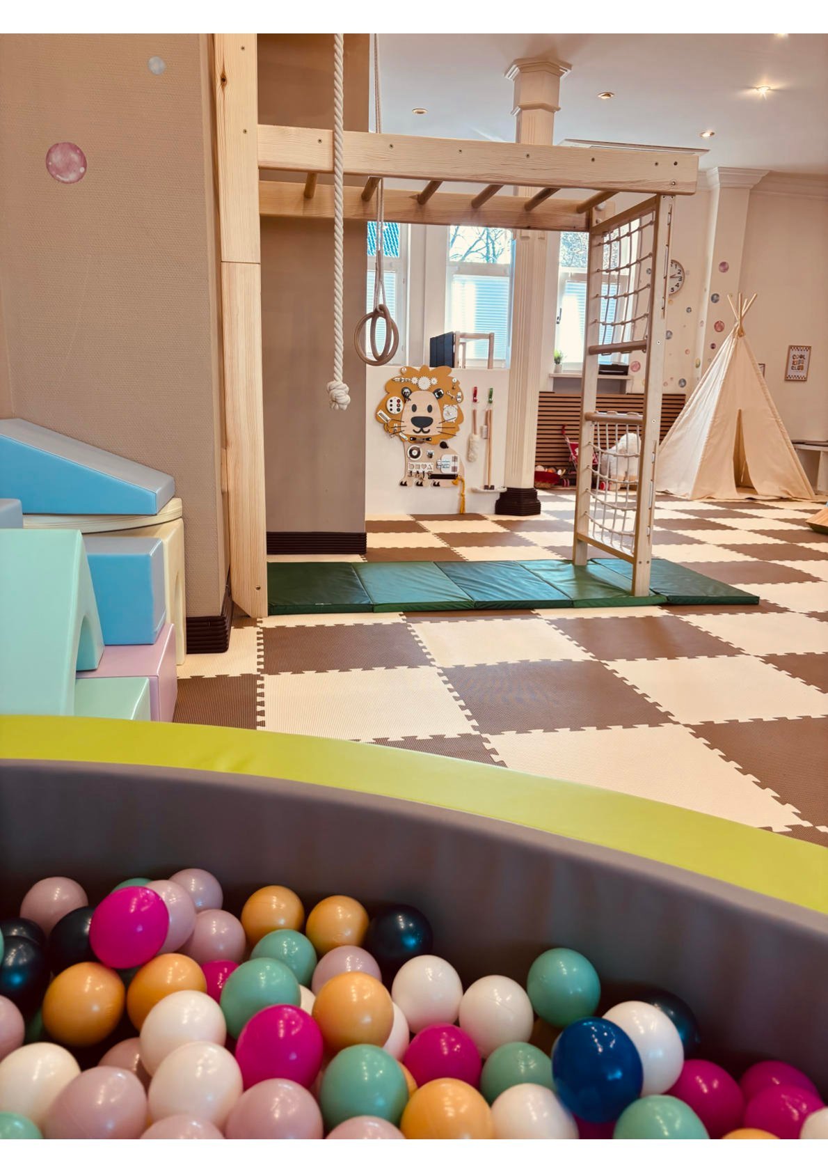 Ein Spielzimmer für Kinder mit einer Kletterstruktur, Schaukeln, einem Tipi-Zelt und einem Ballgraben.