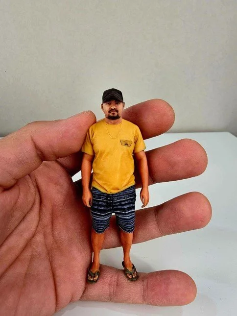 A person holding a tiny figurine of a man with a yellow T-shirt, blue shorts, and flip-flops.