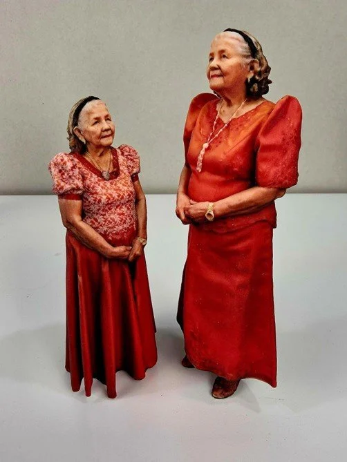 Two elderly women dressed in red standing and facing each other against a plain background.