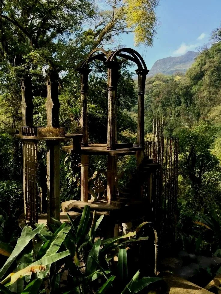 Una estructura de madera antigua en medio de un bosque con árboles y montañas al fondo.