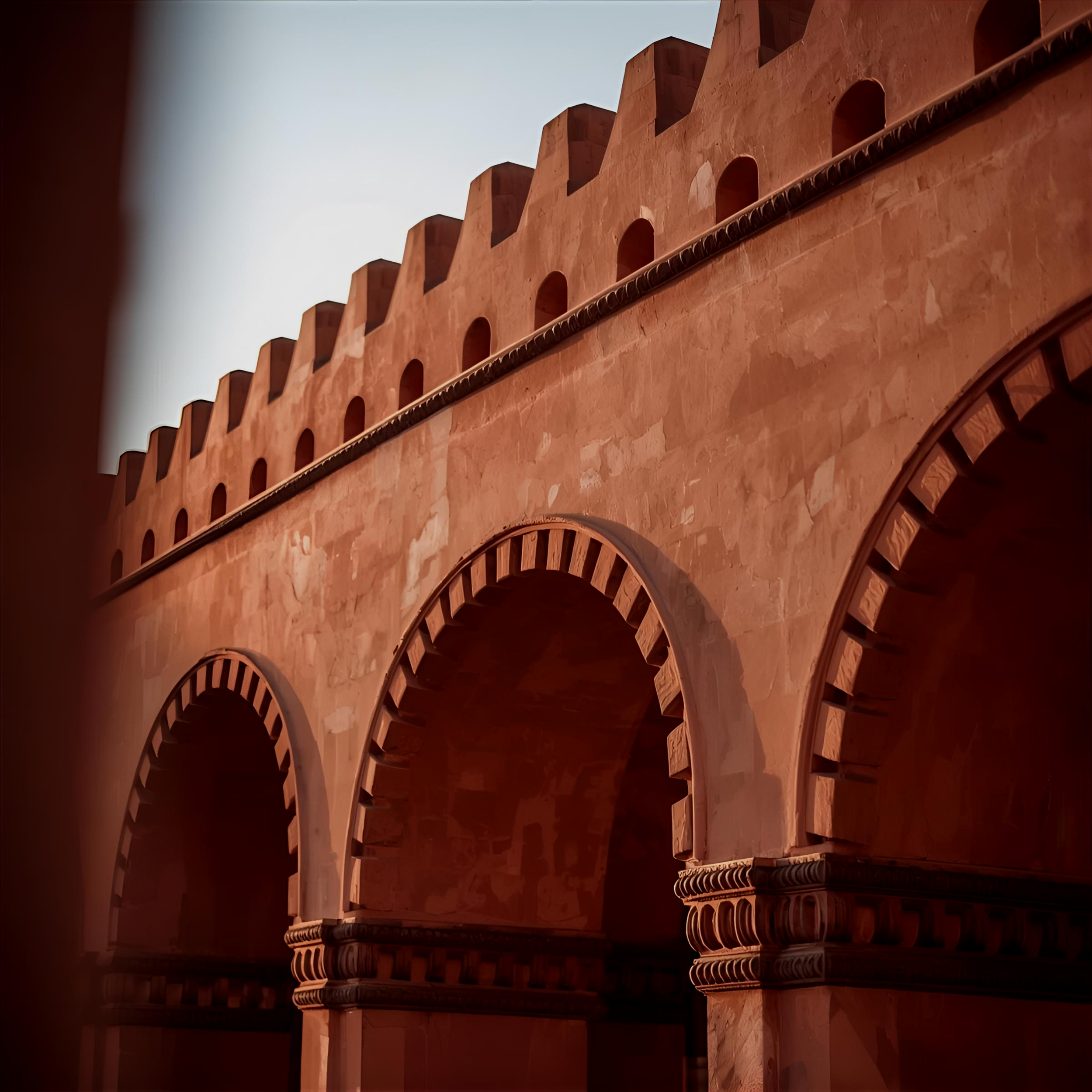 Vista artística de un edificio con arcos de color rojo, con detalles arquitectónicos en las columnas y una serie de ventanas en la parte superior, vista desde abajo.