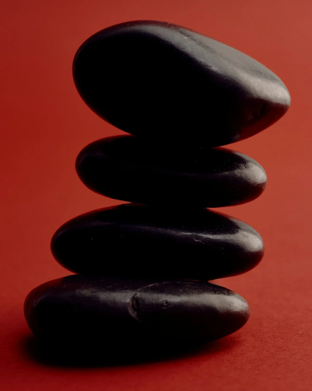 Four smooth black stones stacked vertically against a reddish background.
