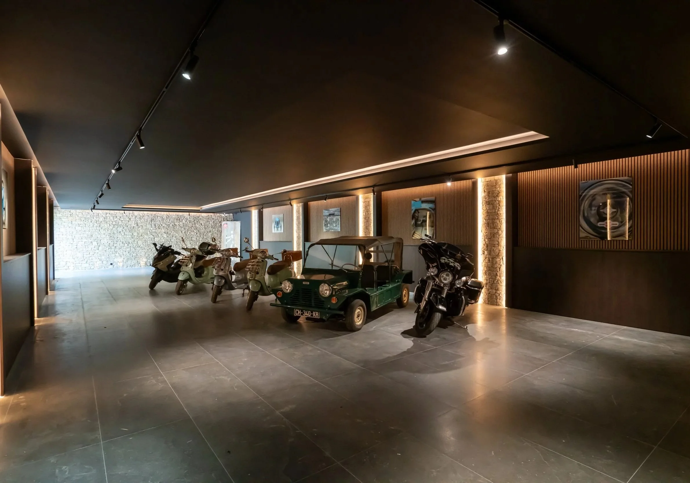 Indoor parking area displaying six scooters, one golf cart, and one motorcycle, with artwork on the walls and a brick wall at the back.