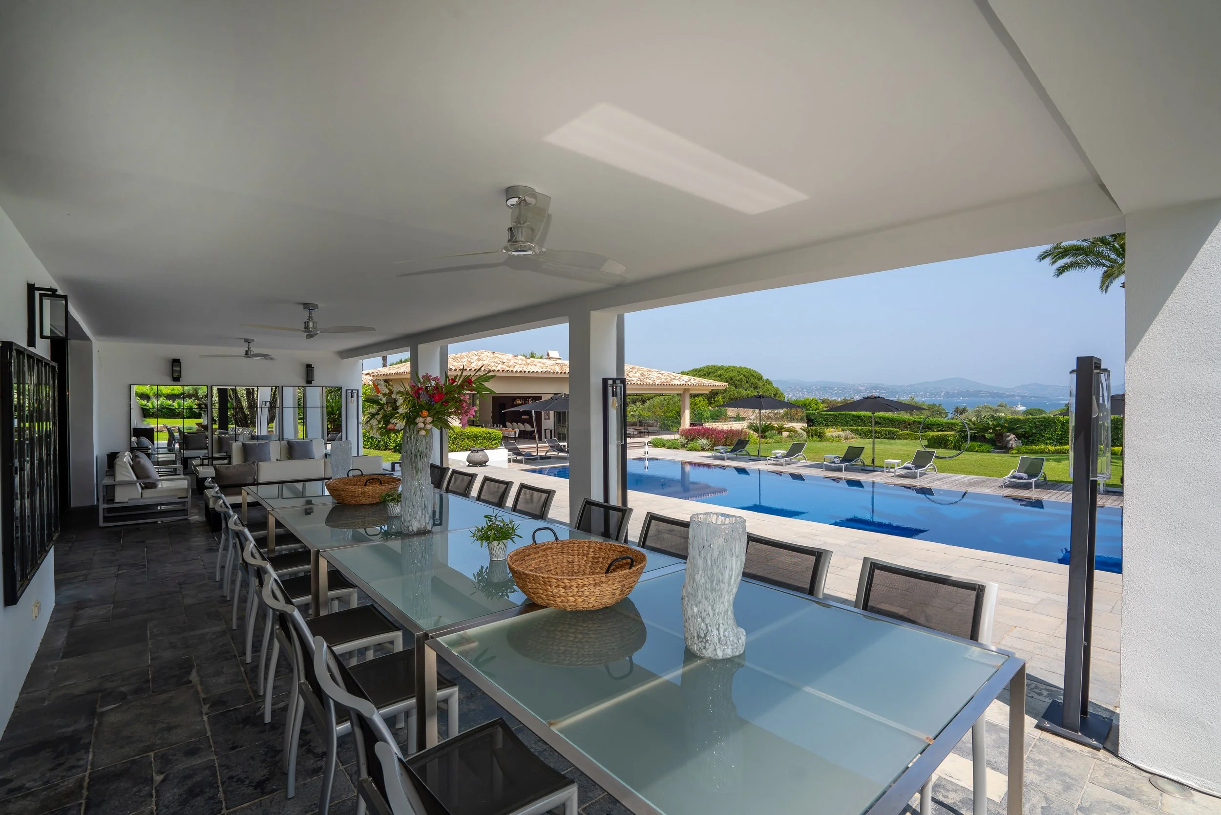 Indoor dining area with a glass table, chairs, and decorative vases, overlooking an outdoor pool and landscape.