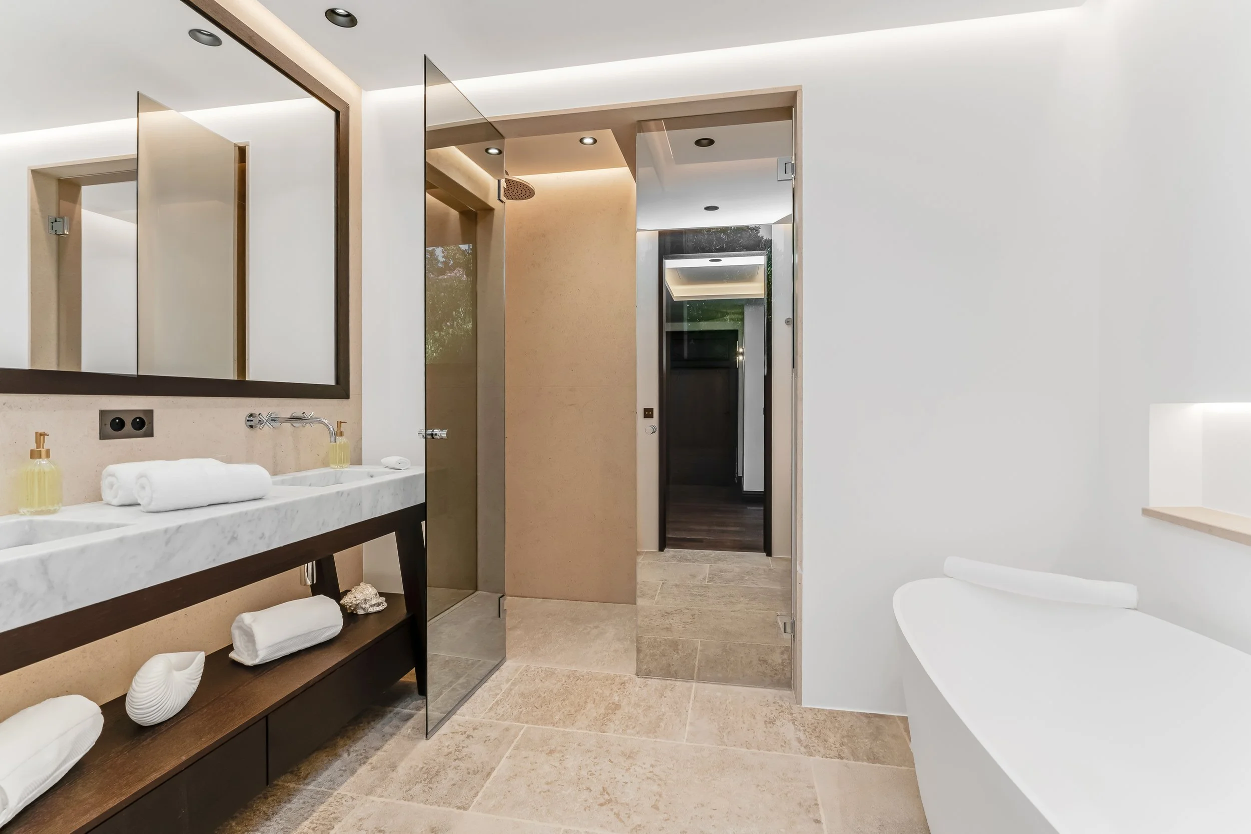 Modern bathroom with a double sink vanity, large mirror, and a walk-in shower, adjacent to a white bathtub, with neutral-toned tile flooring and minimalist decor.