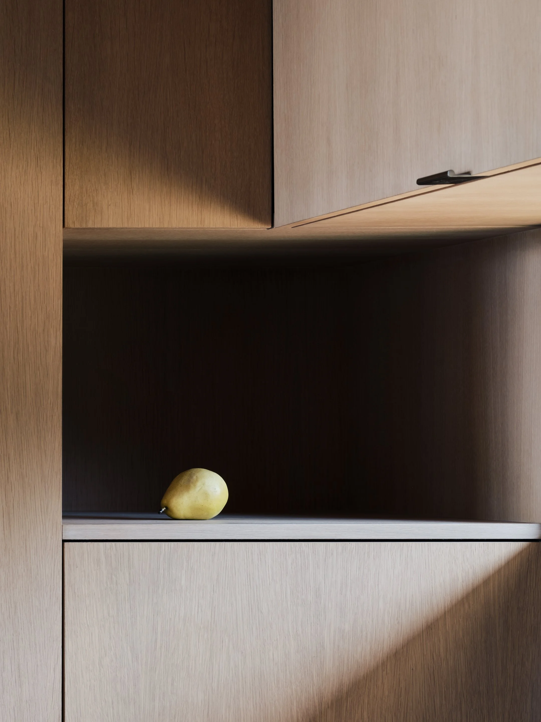 A yellow pear sitting on a wooden shelf within a minimalist wooden cabinet.