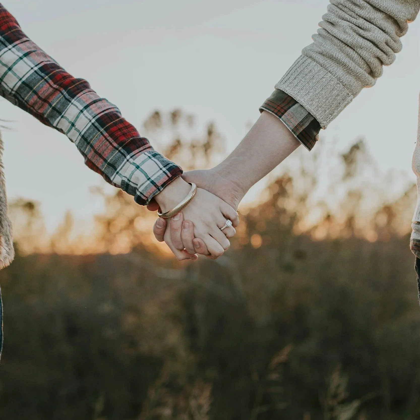 Two people holding hands outdoors during sunset, wearing plaid shirts.