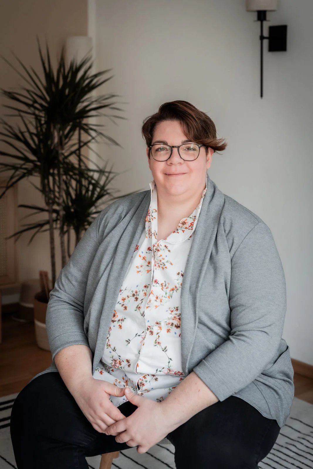 Coach in hellem Praxisraum sitzt auf einem Stuhl und lächelt – ruhige, einladende Atmosphäre für Somatic Experiencing® und systemisches Coaching.