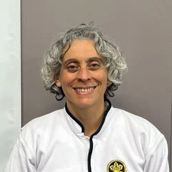 A woman with curly gray hair wearing a white Aikido uniform