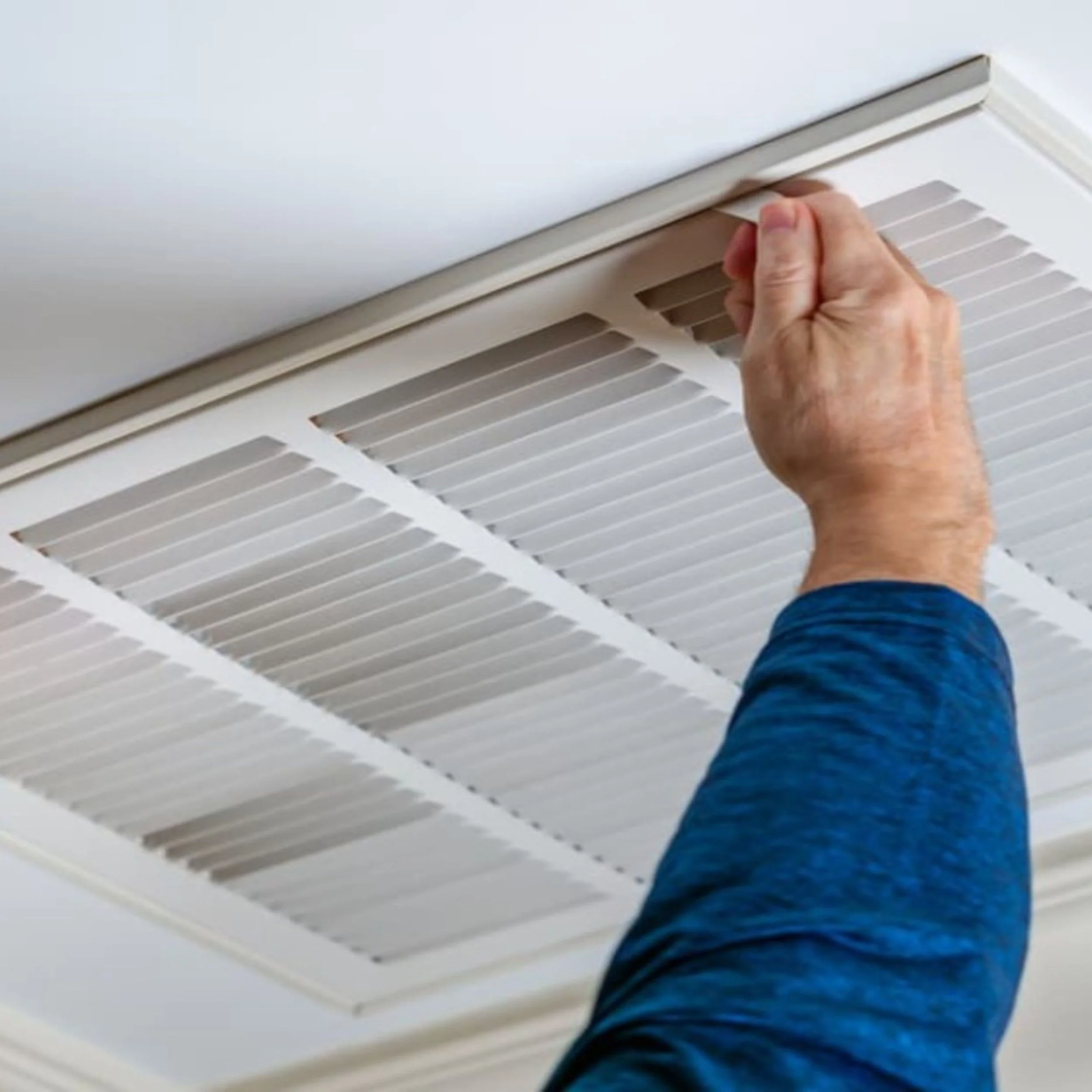 Person cleaning a ceiling vent with a hand.