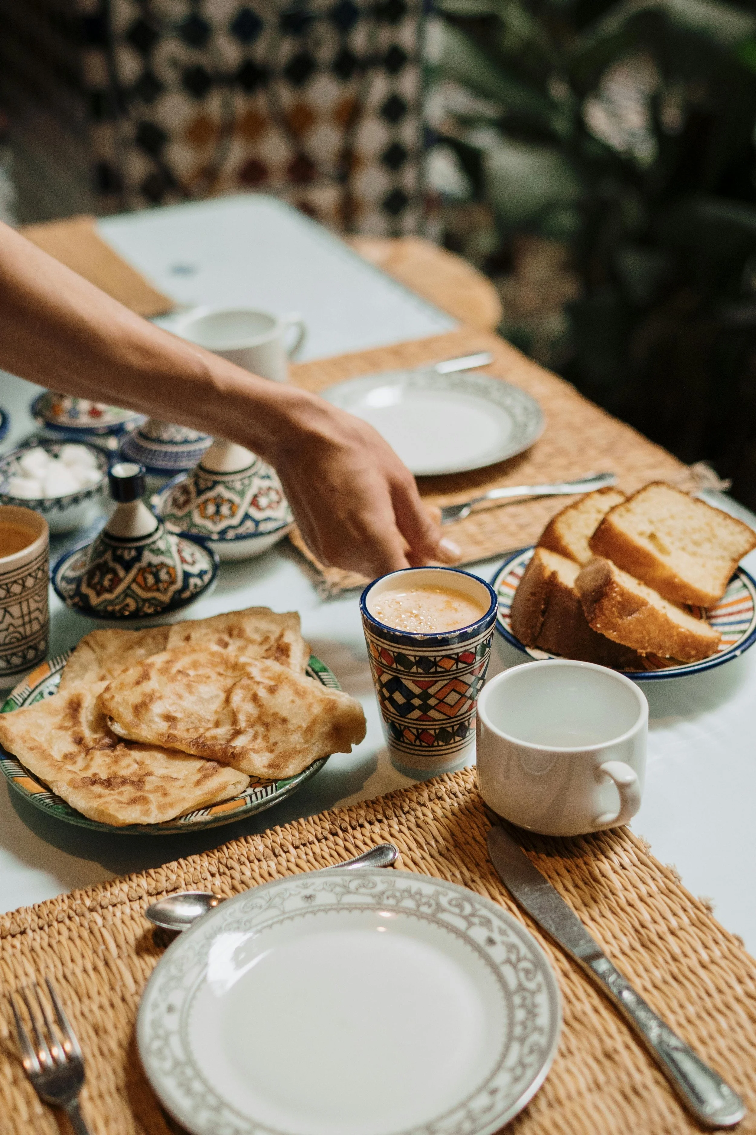 A Moroccan-style breakfast setup with flatbread, sliced cake, a glass of tea, and Moroccan tea pots on a decorated table.