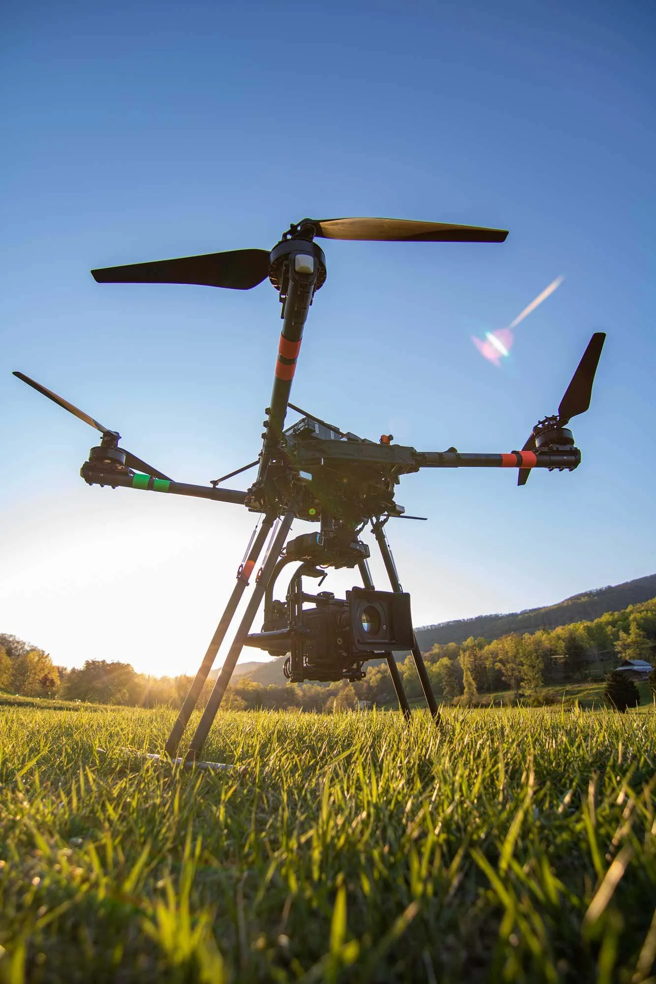 A drone with a camera attached flying low over a grassy field during sunset.
