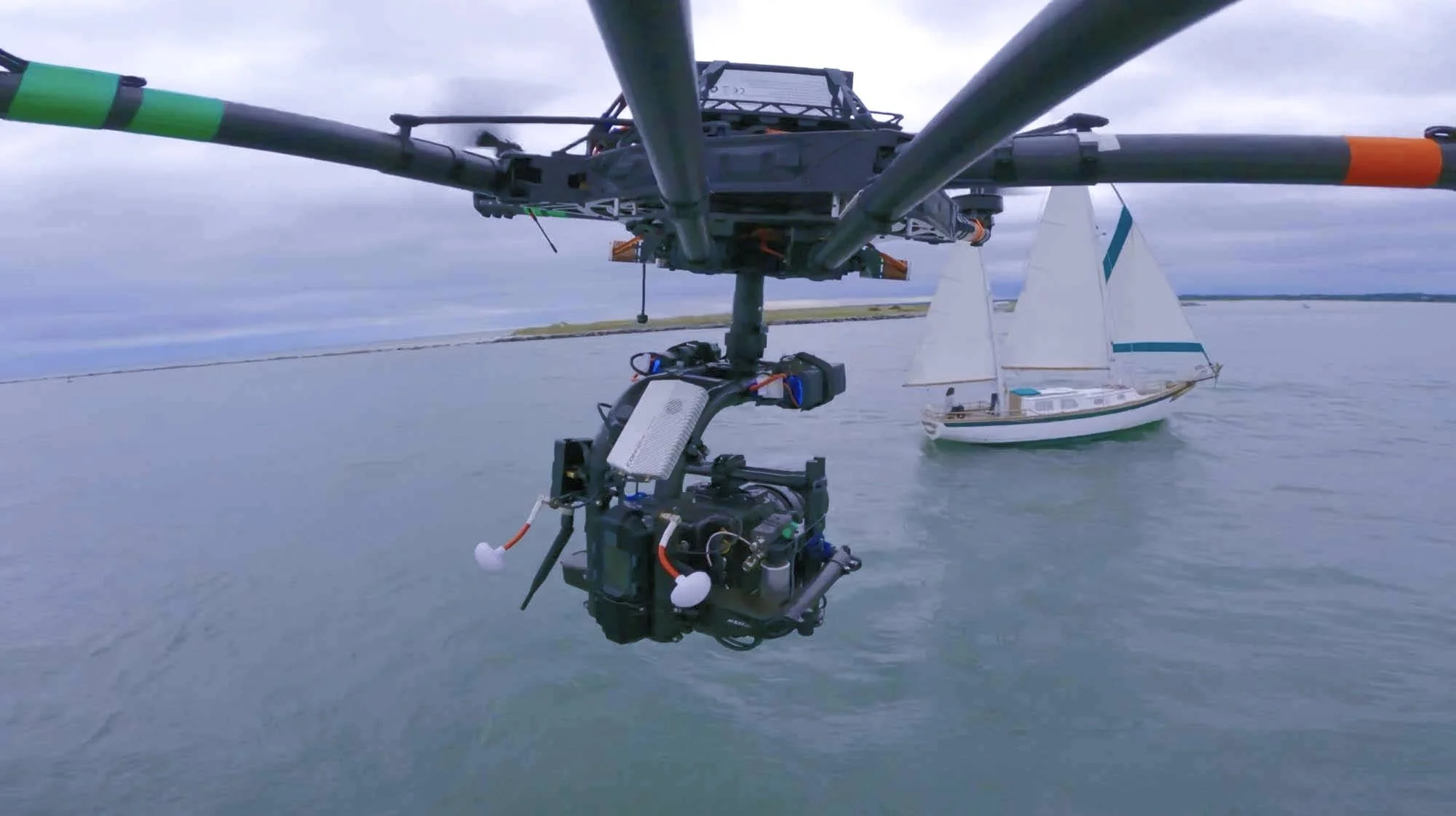 Close-up of a drone filming a sailboat on a body of water during cloudy weather.