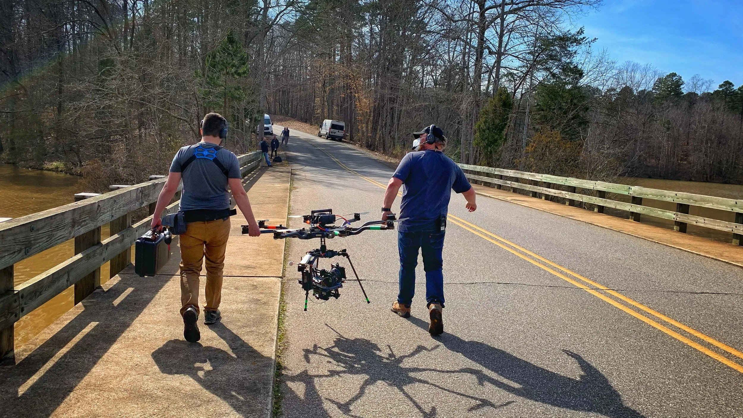Two people walking on a bridge with a drone flying in the air.