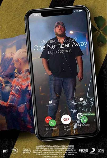 iPhone screen displaying an incoming call from Luke Combs with a cracked screen and a photo of him in casual clothes. A magazine or photo book is partially visible underneath.