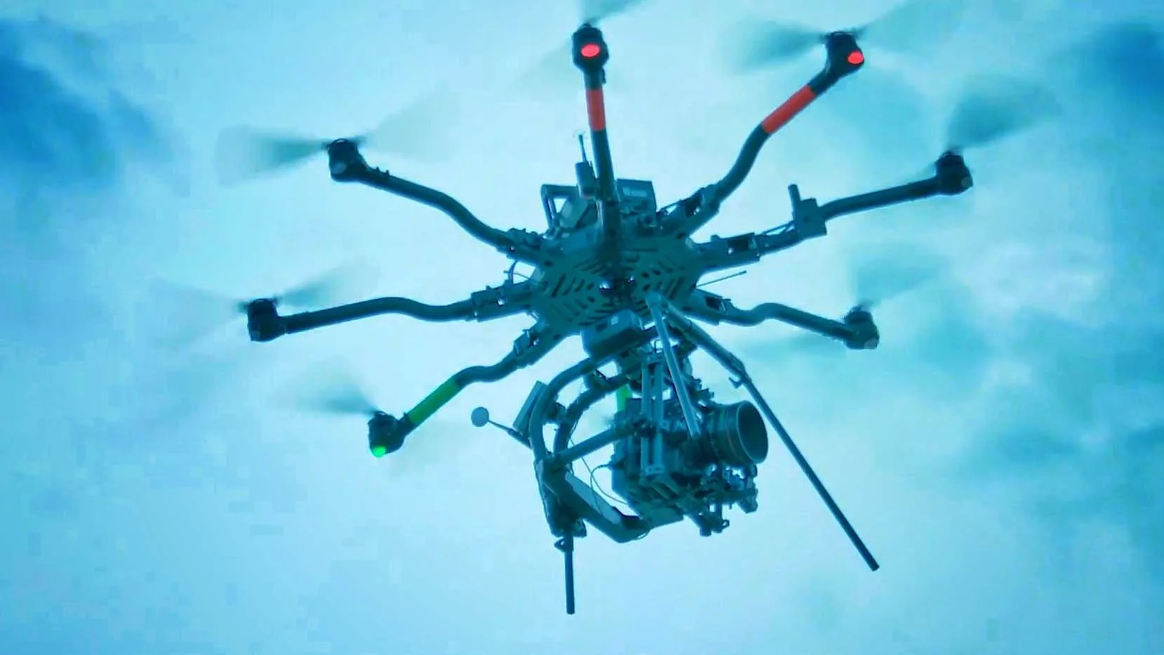 A drone with multiple extended arms and rotors flying in a cloudy sky.