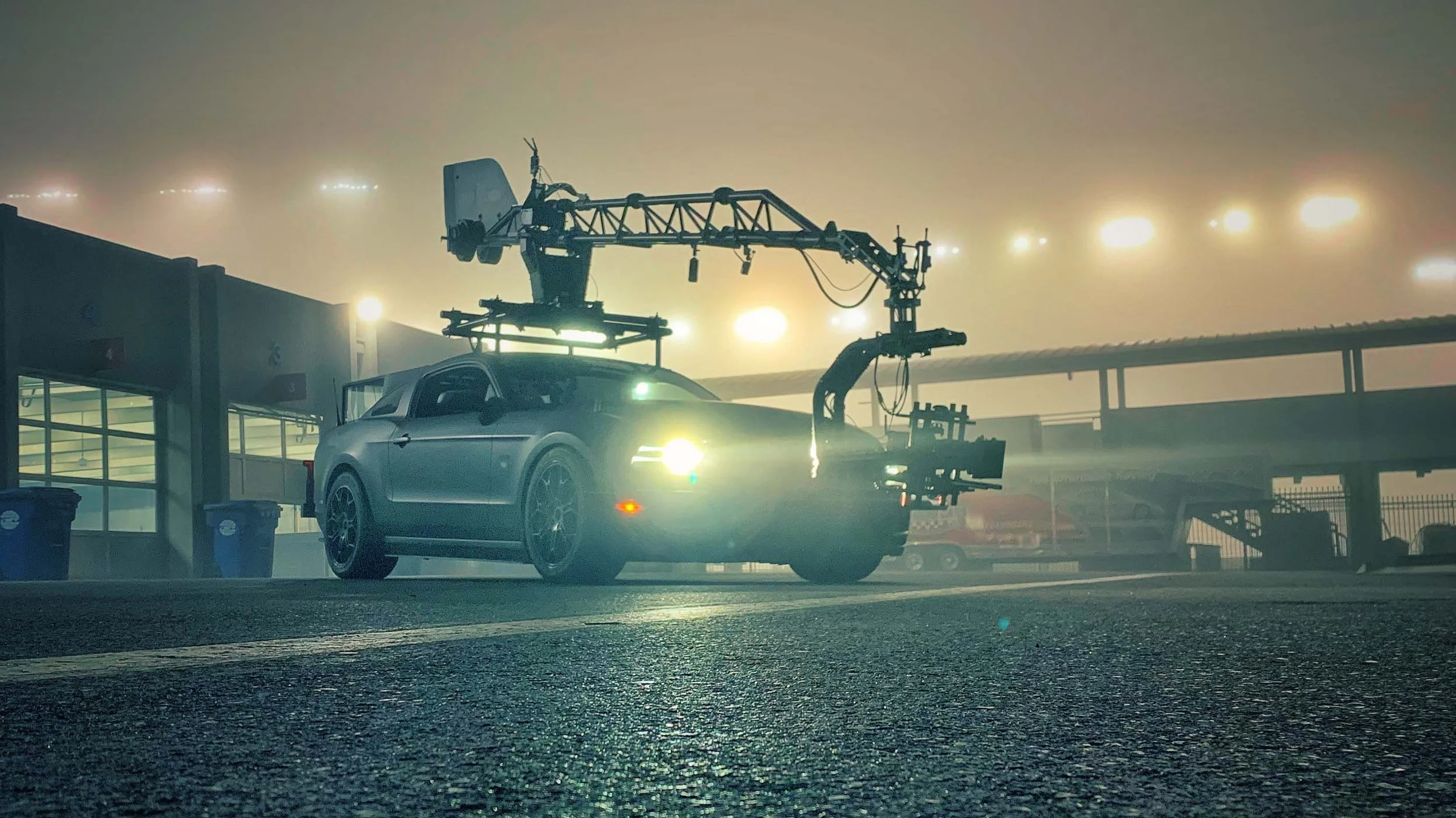 A film camera mounted on a vehicle in a foggy or smoky environment with bright lights in the background.