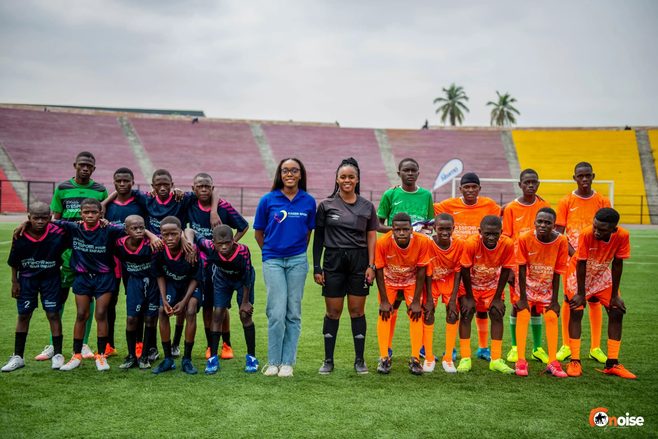 A youth soccer team with coaches standing on a soccer field before a game, with a stadium and palm trees in the background.