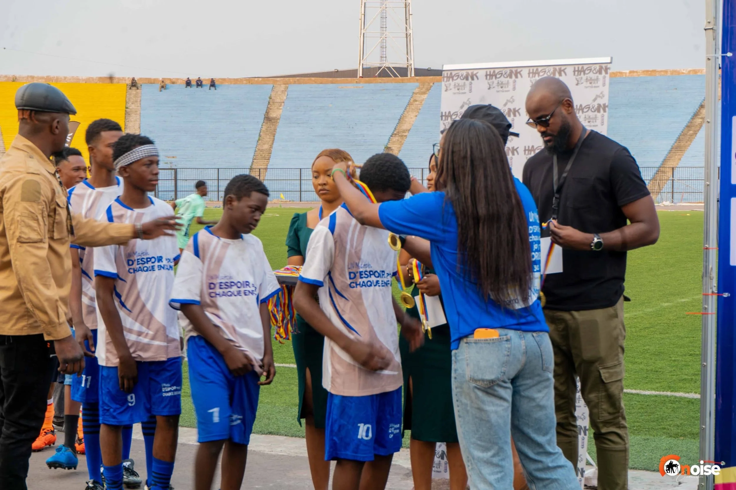 Children in soccer uniforms receiving medals from adults on a soccer field during an award ceremony.