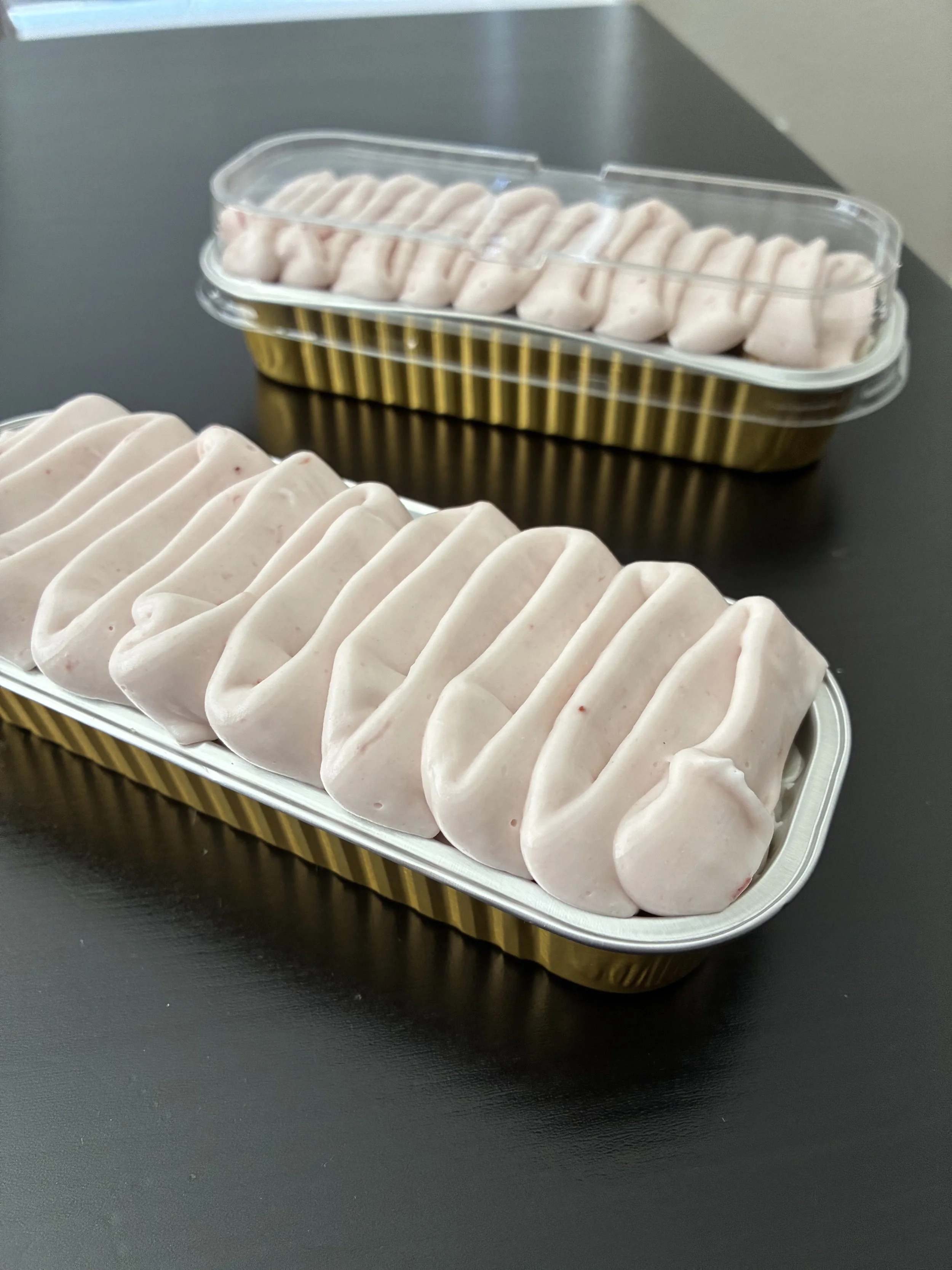 Two containers of pink marshmallows on a black surface.