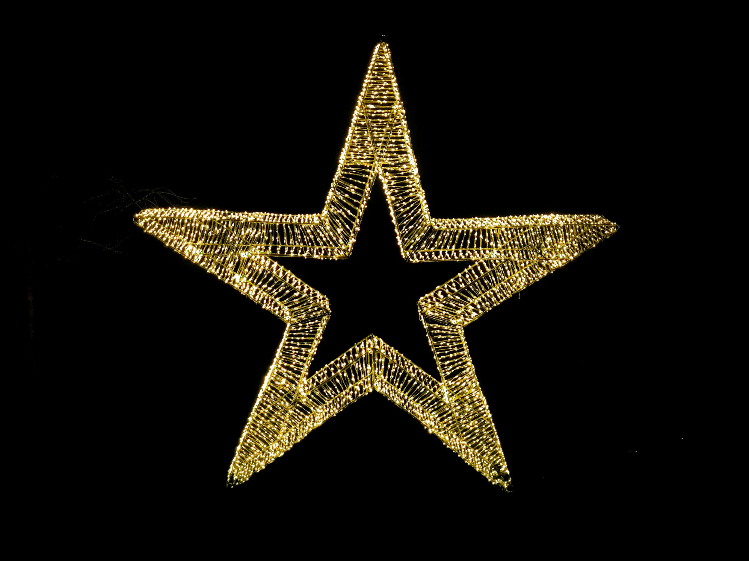 Gold star-shaped Christmas light decoration against a black background.