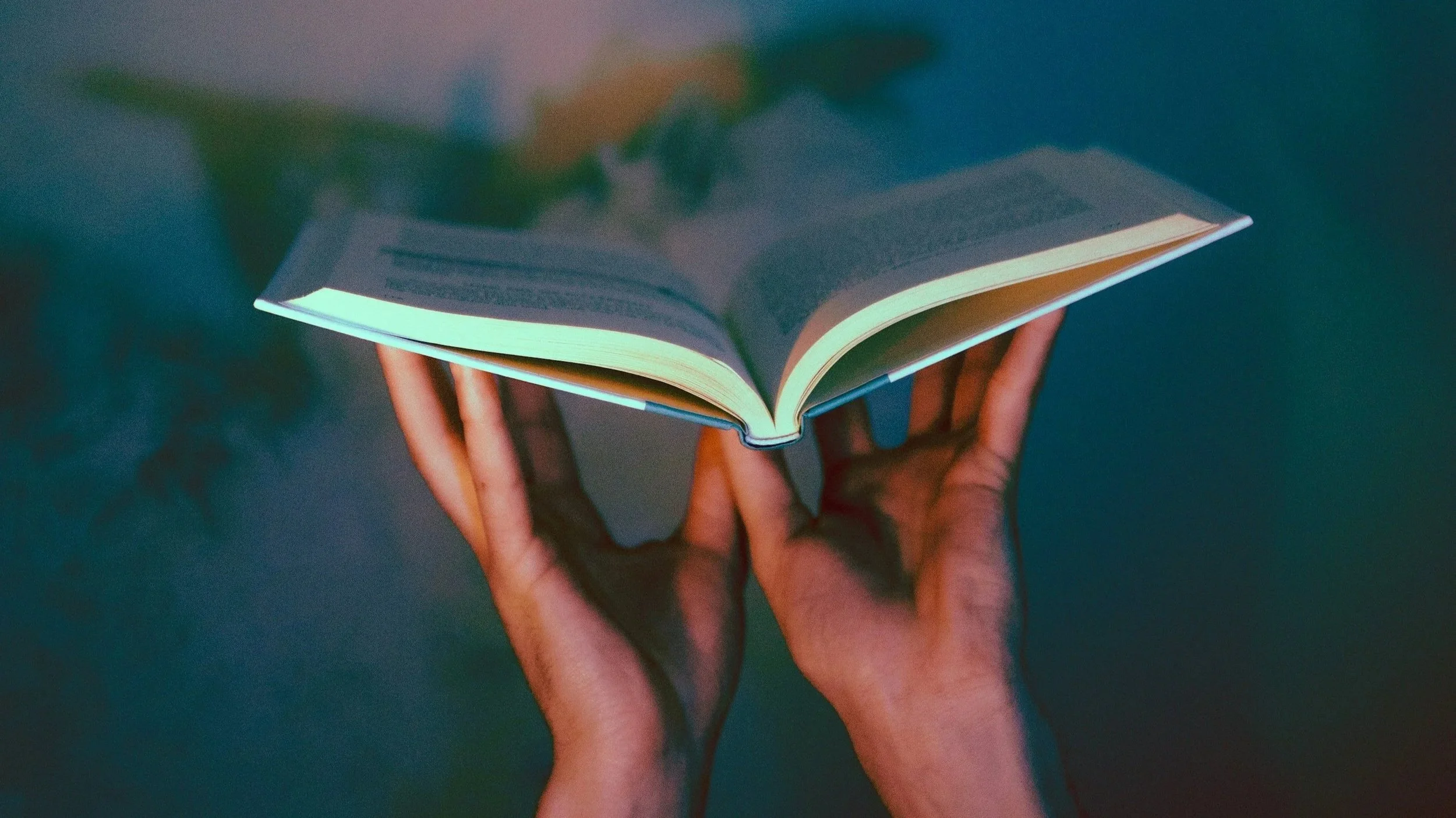 Hands holding an open book with pages glowing slightly, against a dark, blurred background. Psychic readings for the future.