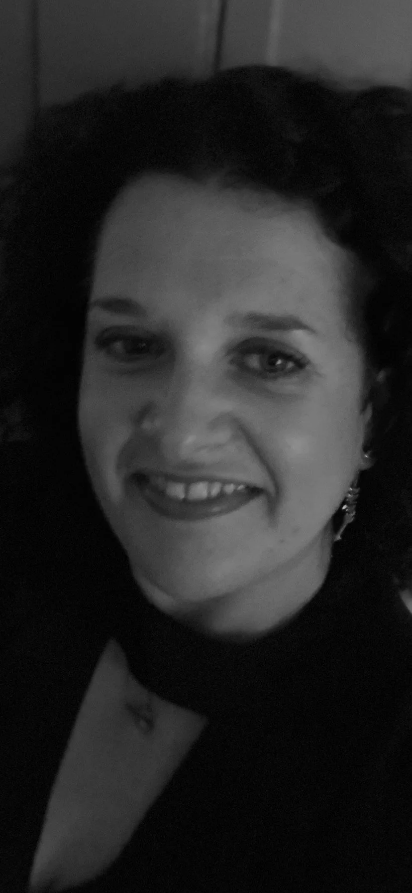 Black and white close-up photo of a woman smiling, wearing earrings, with her hair styled back. Melissa O'Sullivan psychic medium from Worcestershire.