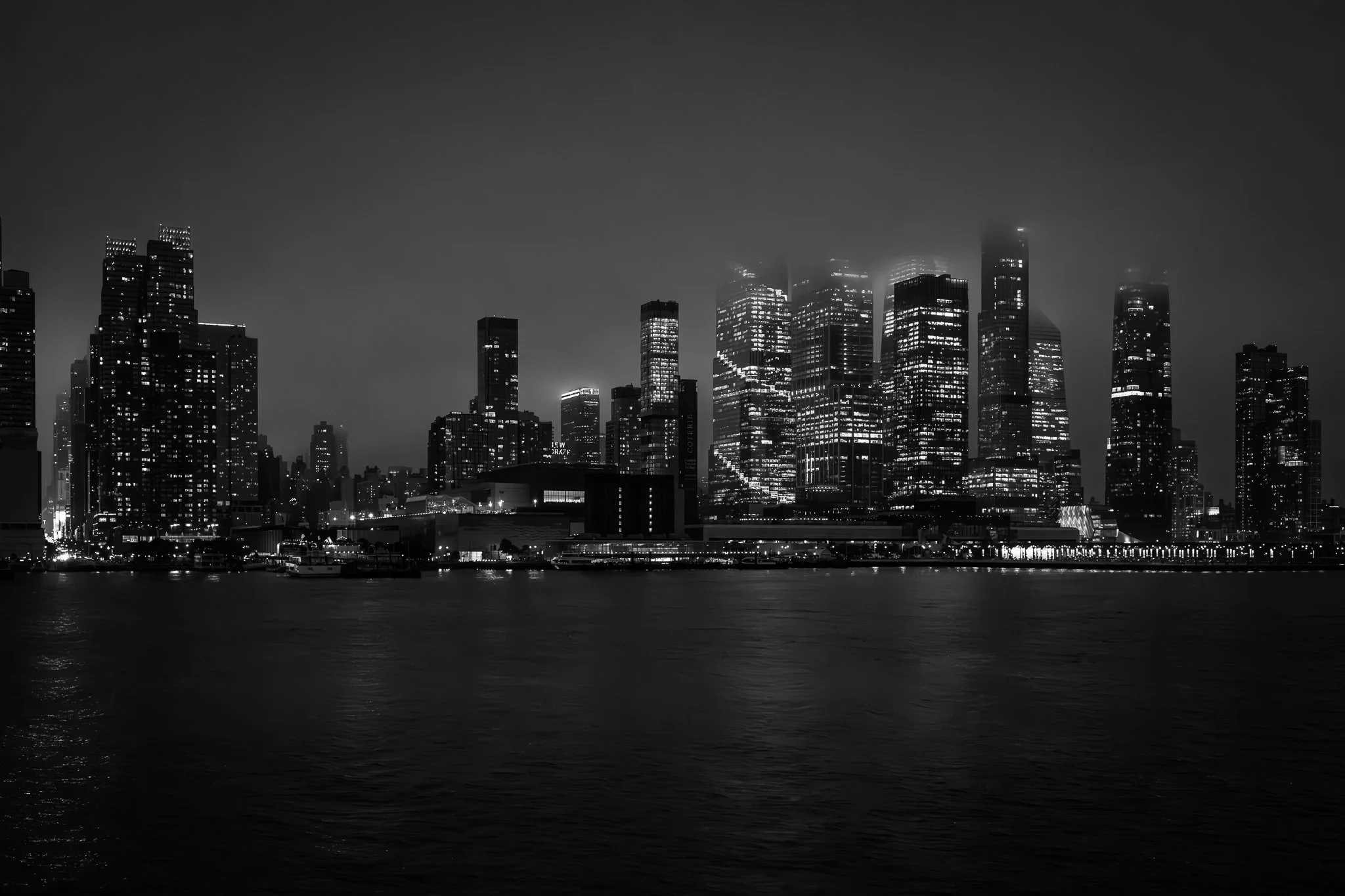 Nighttime black and white photo of a city skyline with illuminated skyscrapers reflected on the water.