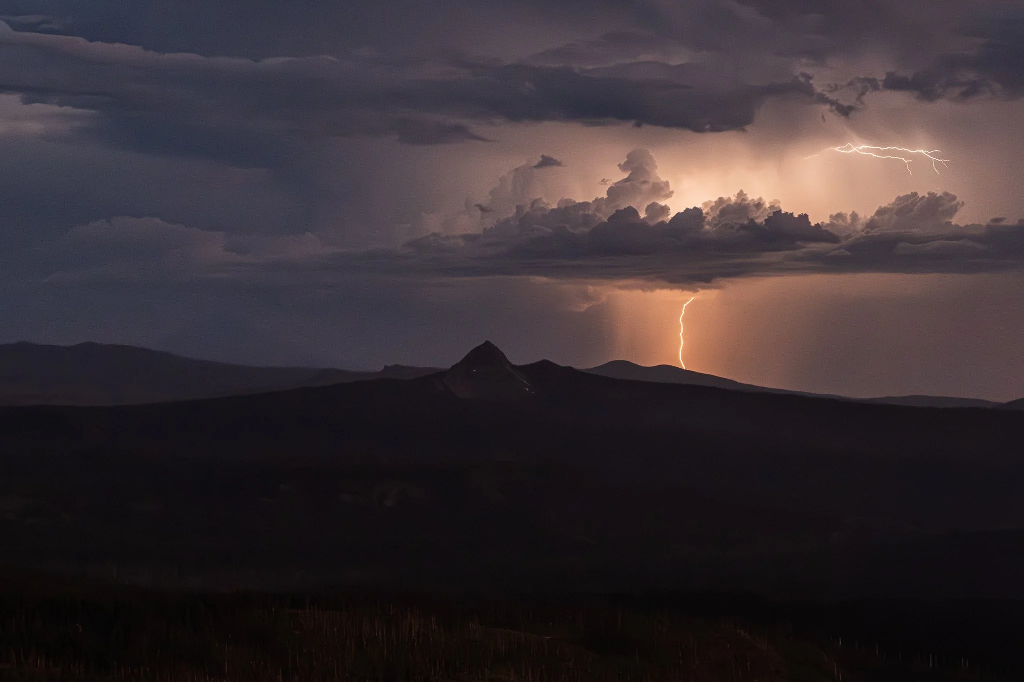 A lightning bolt strikes in a stormy sky over mountains at night.