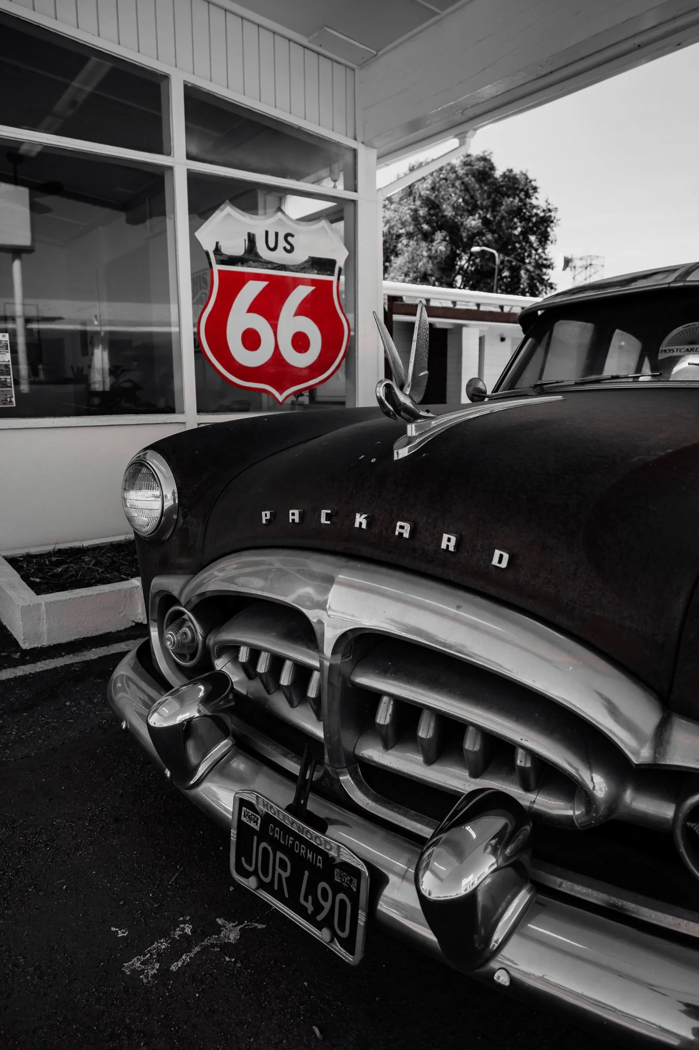 A black and white vintage Packard car with a California license plate JQR L490, parked outside a building with a large Route 66 sign in the window.