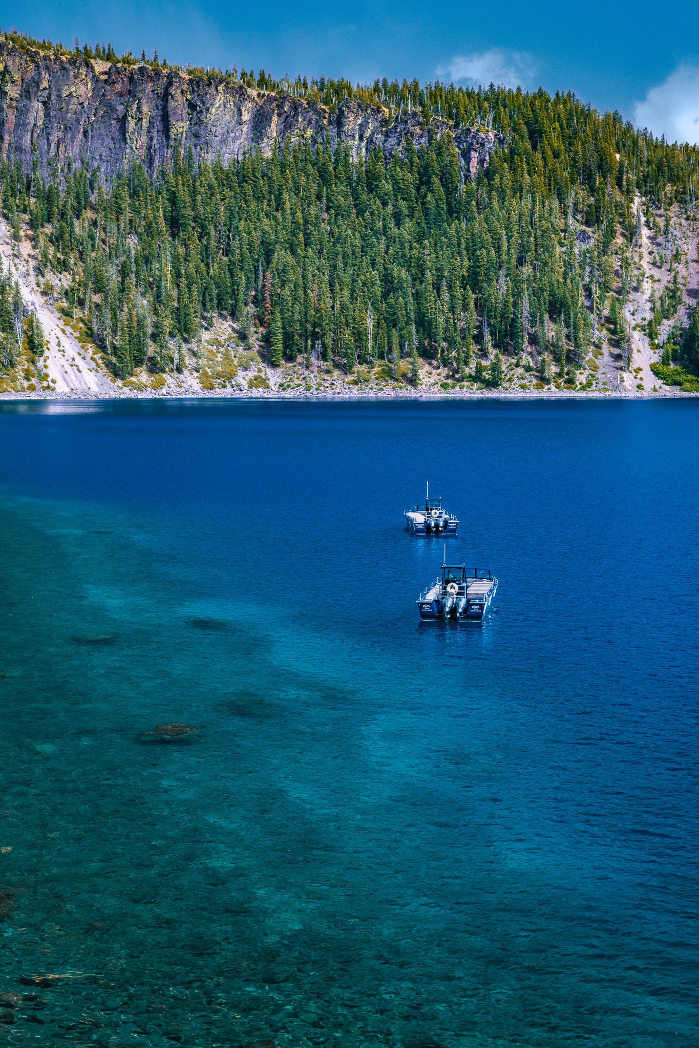 Two boats floating on a clear blue lake with a forested mountain in the background.
