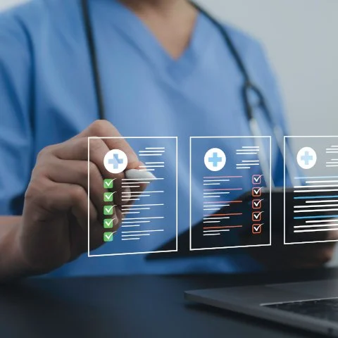 Healthcare professional wearing blue scrubs and a stethoscope showing a digital health report with checkmarks and medical icons.