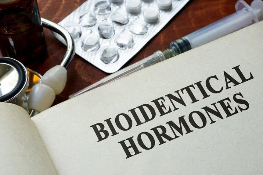 Open book titled 'Biodentical Hormones' on a table with medical items including a stethoscope, a blister pack of pills, and syringes.