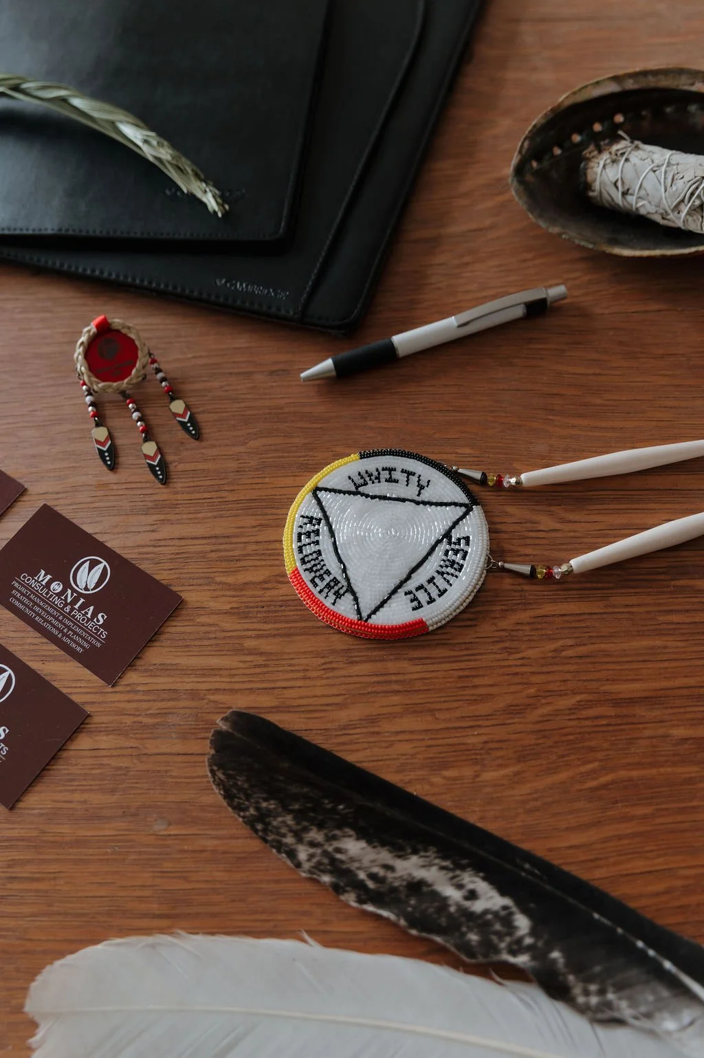 Assorted Native American jewelry and crafts on a wooden surface, including beaded earrings, a beaded circular object with tribal symbols, feathers, and business cards.