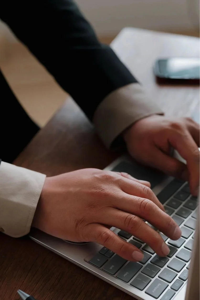 Person in business attire typing on a laptop keyboard at a wooden desk.