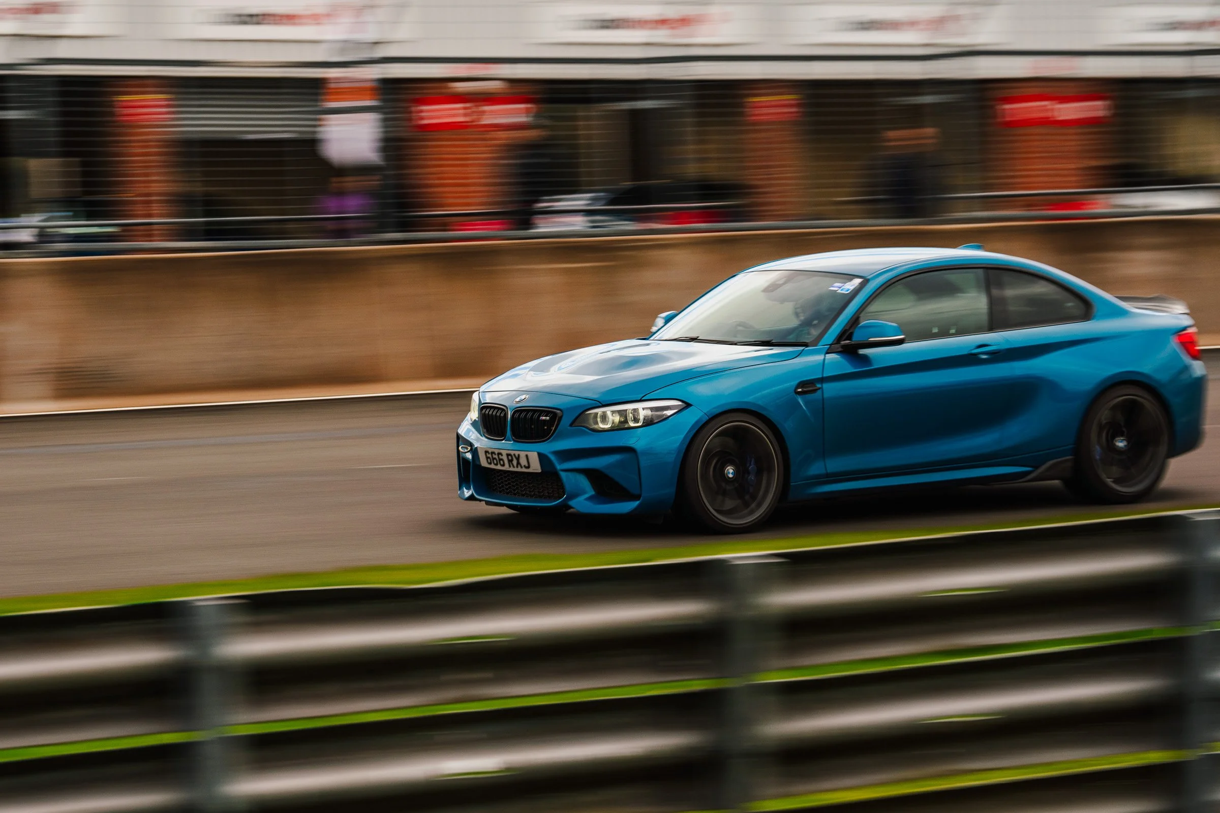 A blue BMW coupe racing on a track with blurred background and foreground, indicating high speed.
