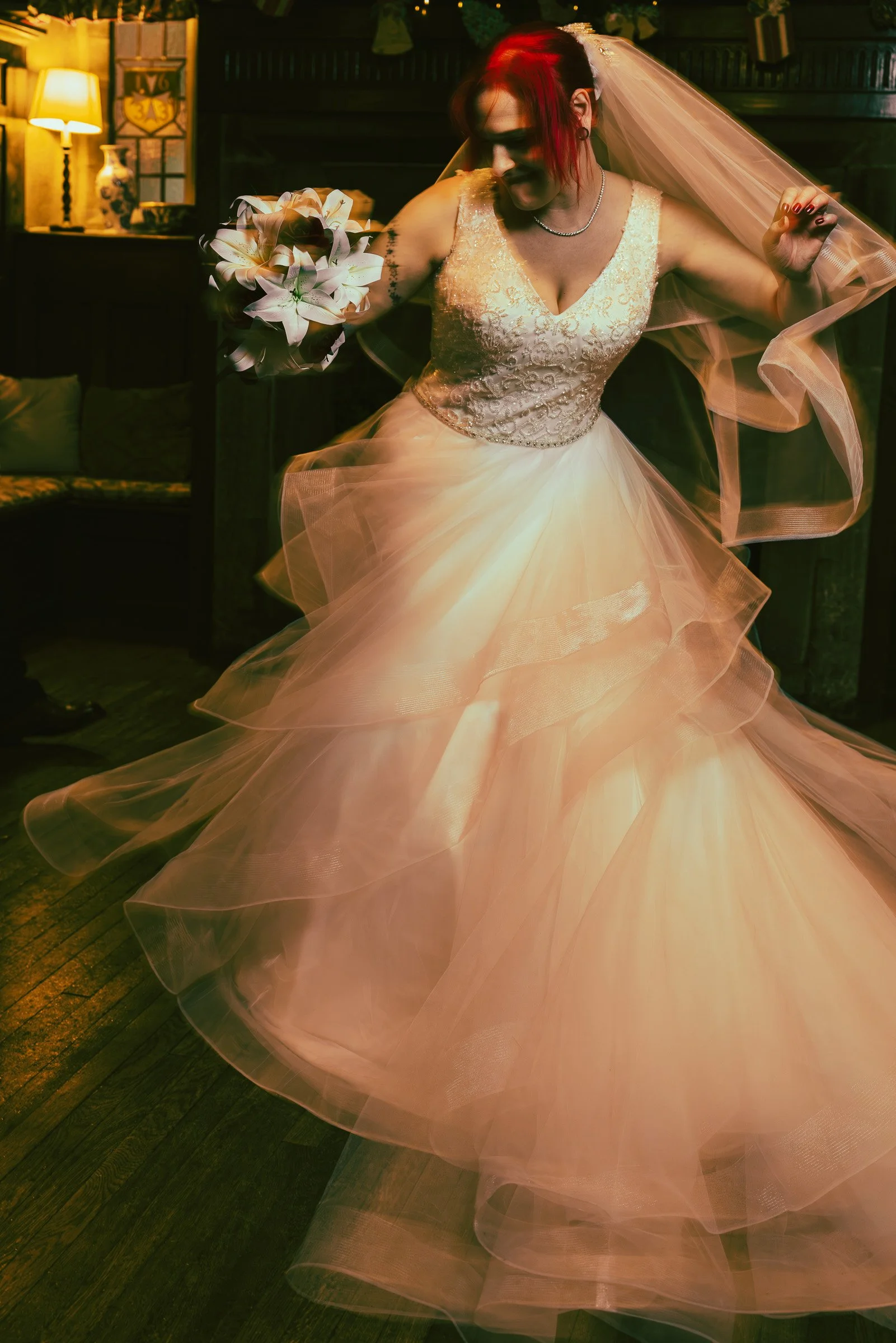 A bride with red hair in a wedding dress dancing with a bouquet in her hand.