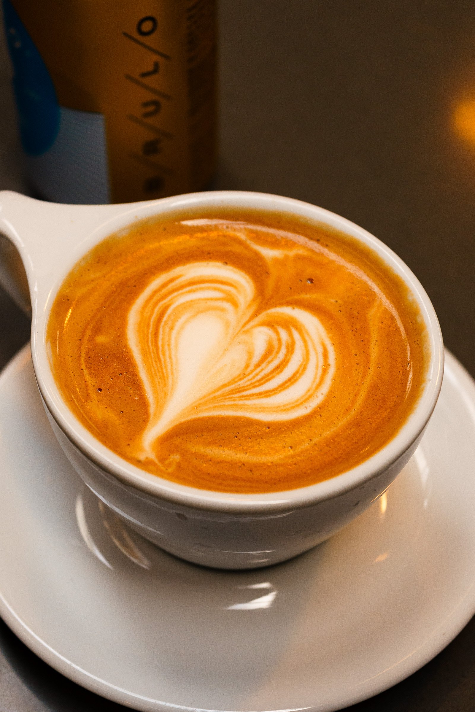 A white coffee cup with latte art on top, sitting on a white saucer.