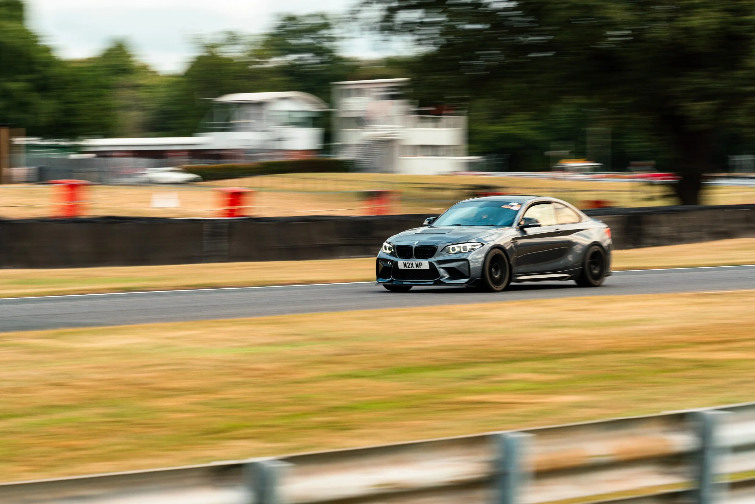 A gray sports car driving on a road with a blurry background of trees and a building.