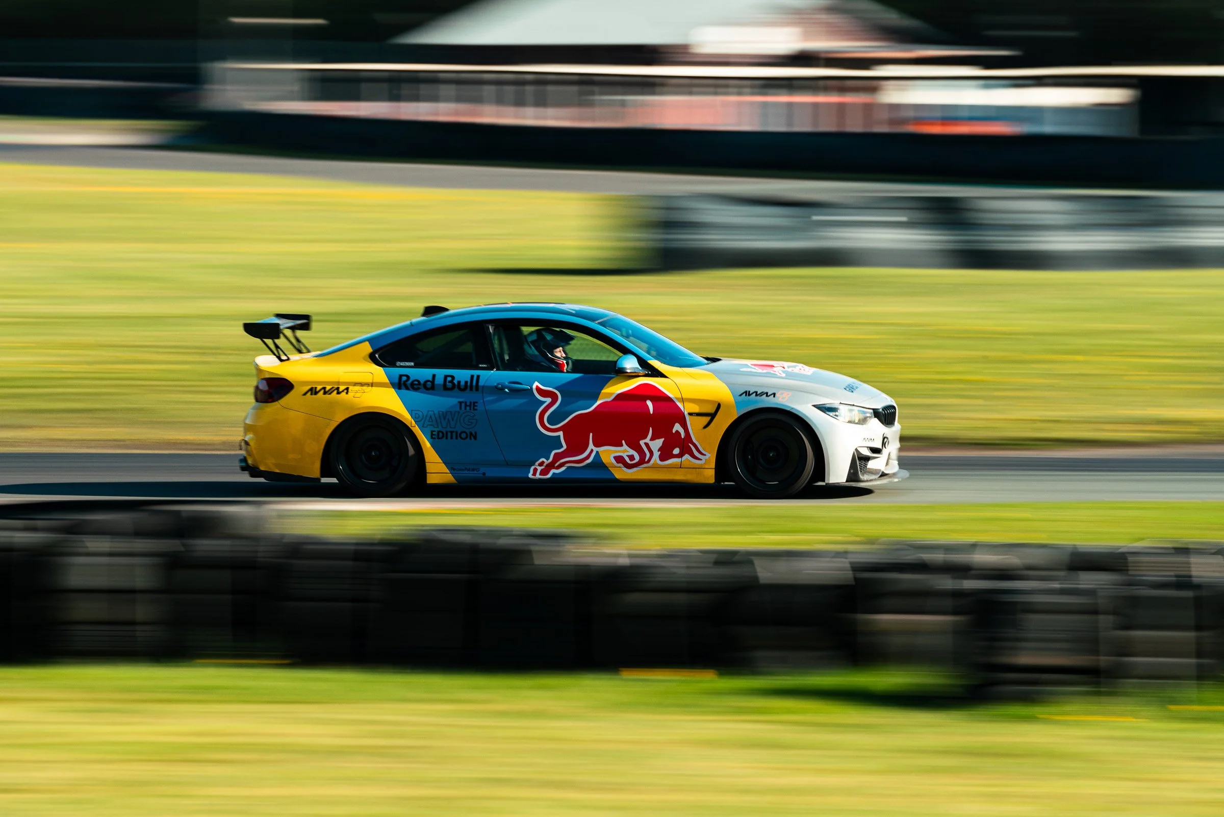 A race car with red bull branding moving at high speed on a race track, with blurred background and foreground indicating motion.
