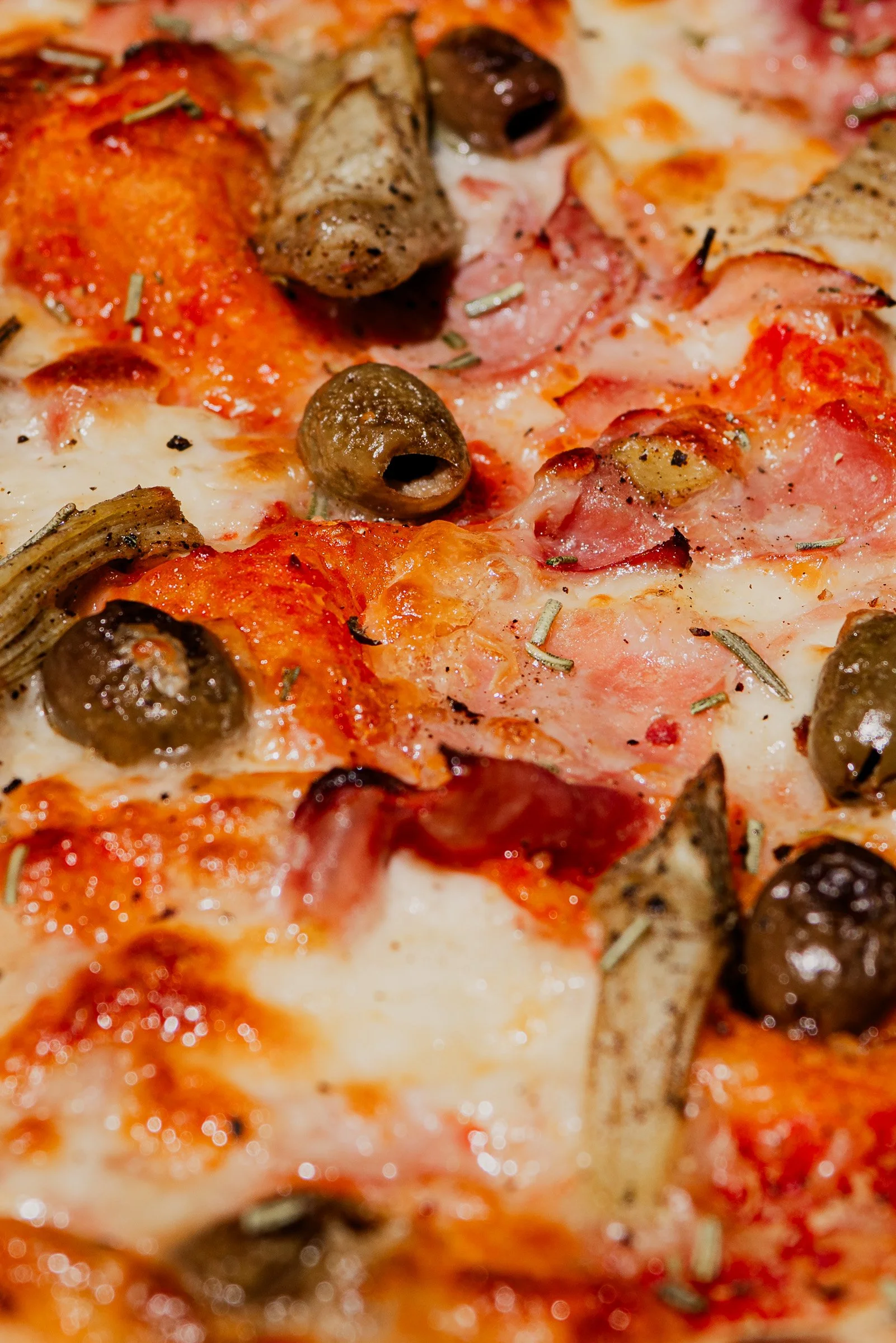 Close-up of a pizza with pepperoni, black olives, sausage, herbs, and melted cheese.