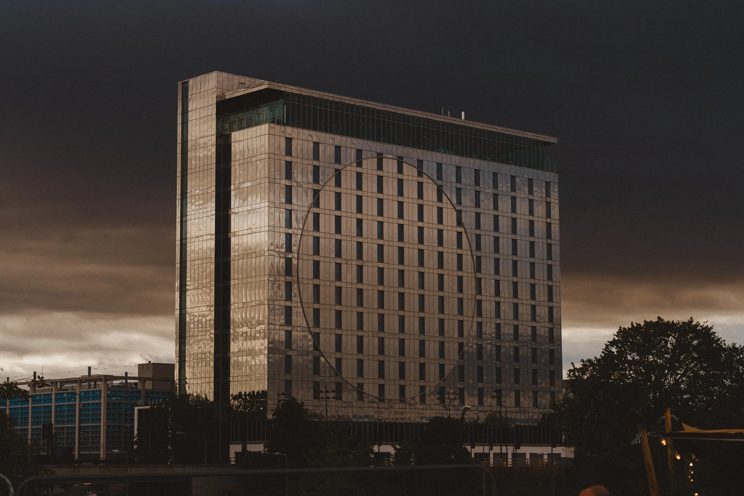 A tall modern building with glass and concrete exterior during sunset.