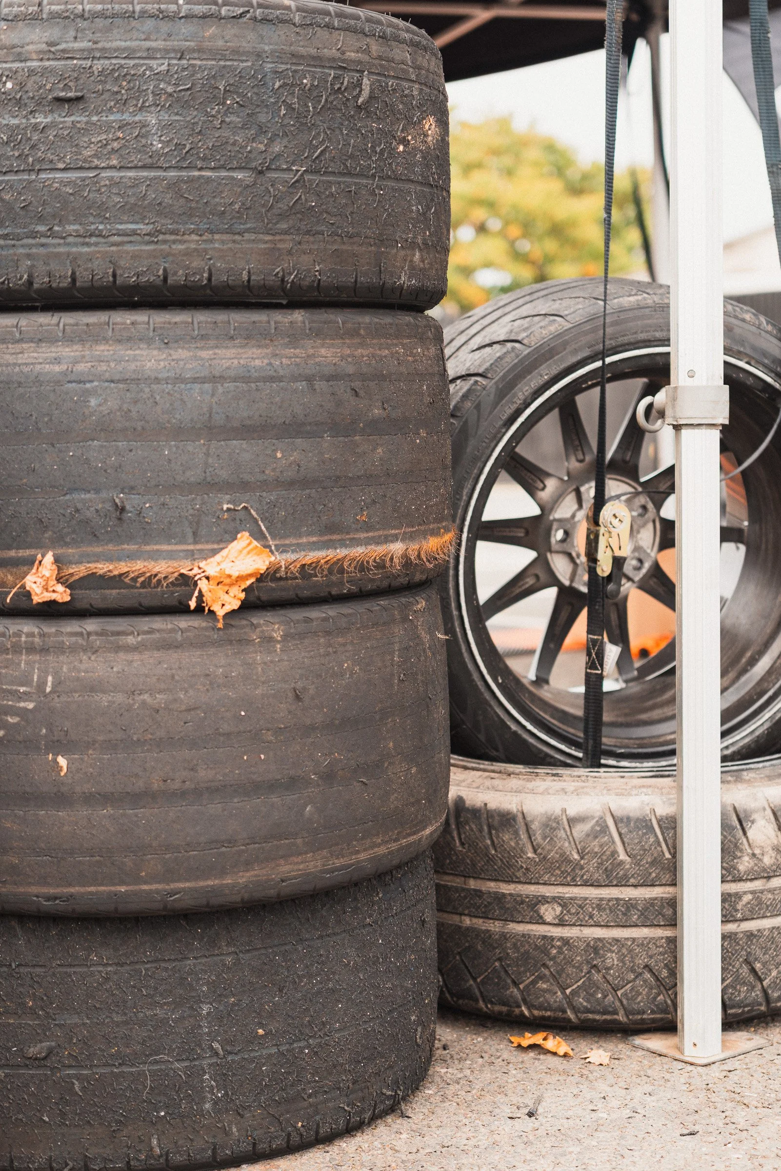 Stack of used tires and a car wheel on a concrete surface, with some autumn leaves nearby.