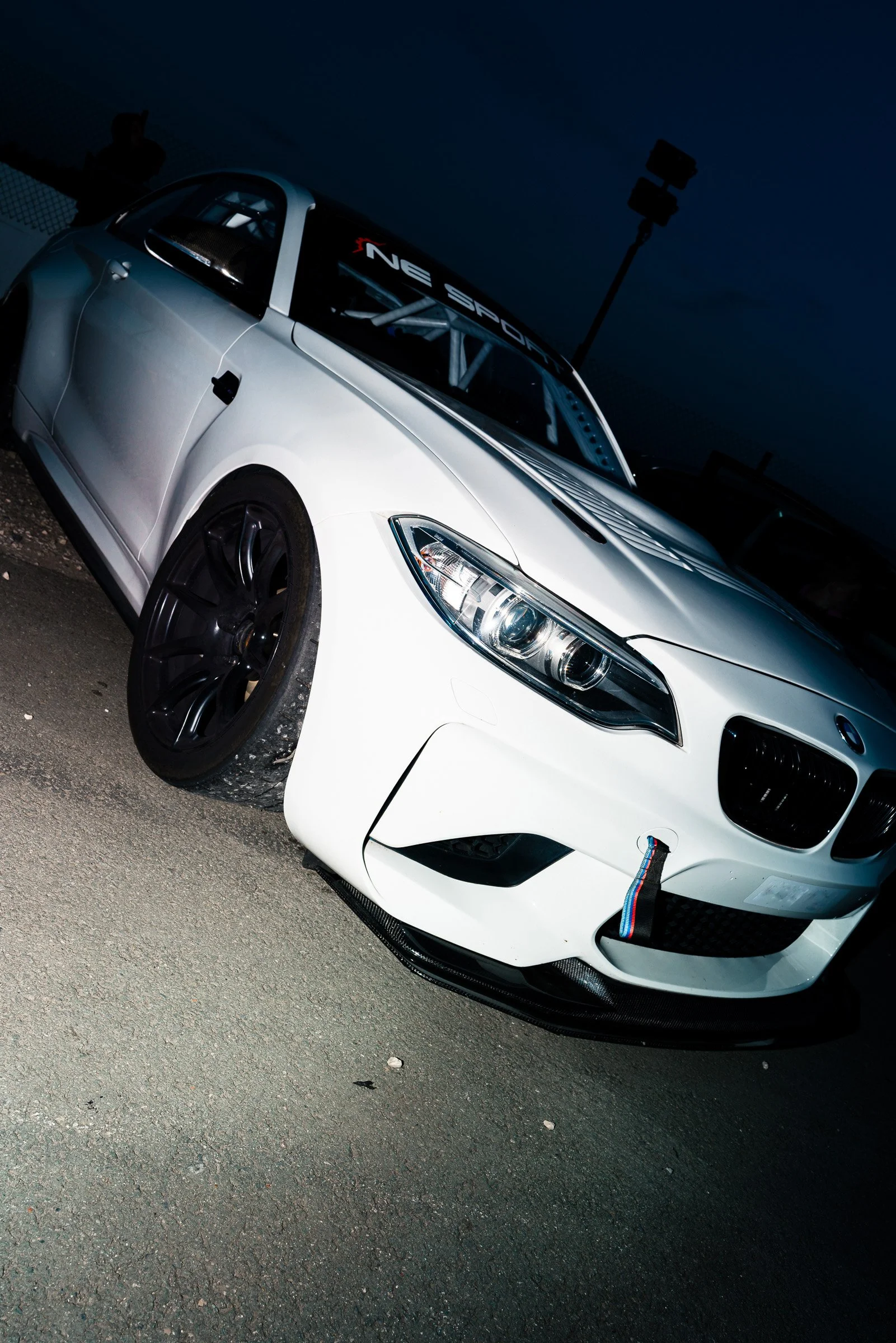 A white sports car with black wheels, parked on an asphalt road at night.