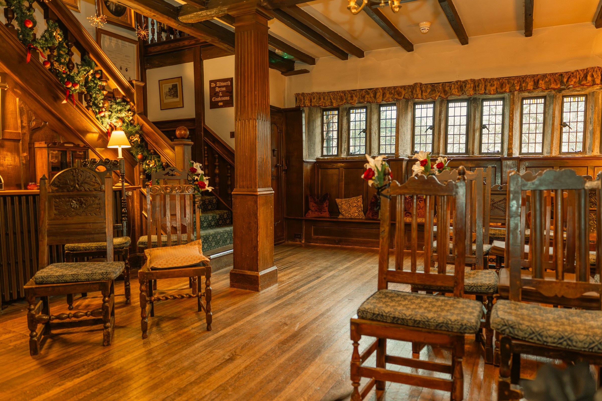 A cozy, vintage-style room decorated for Christmas with wooden furniture, Christmas ornaments, and flowers on chairs.