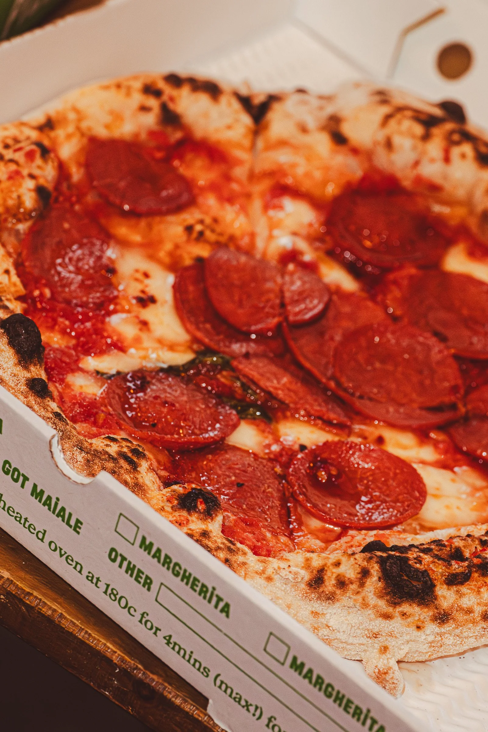 Close-up of a pepperoni pizza in a white pizza box on a wooden surface.