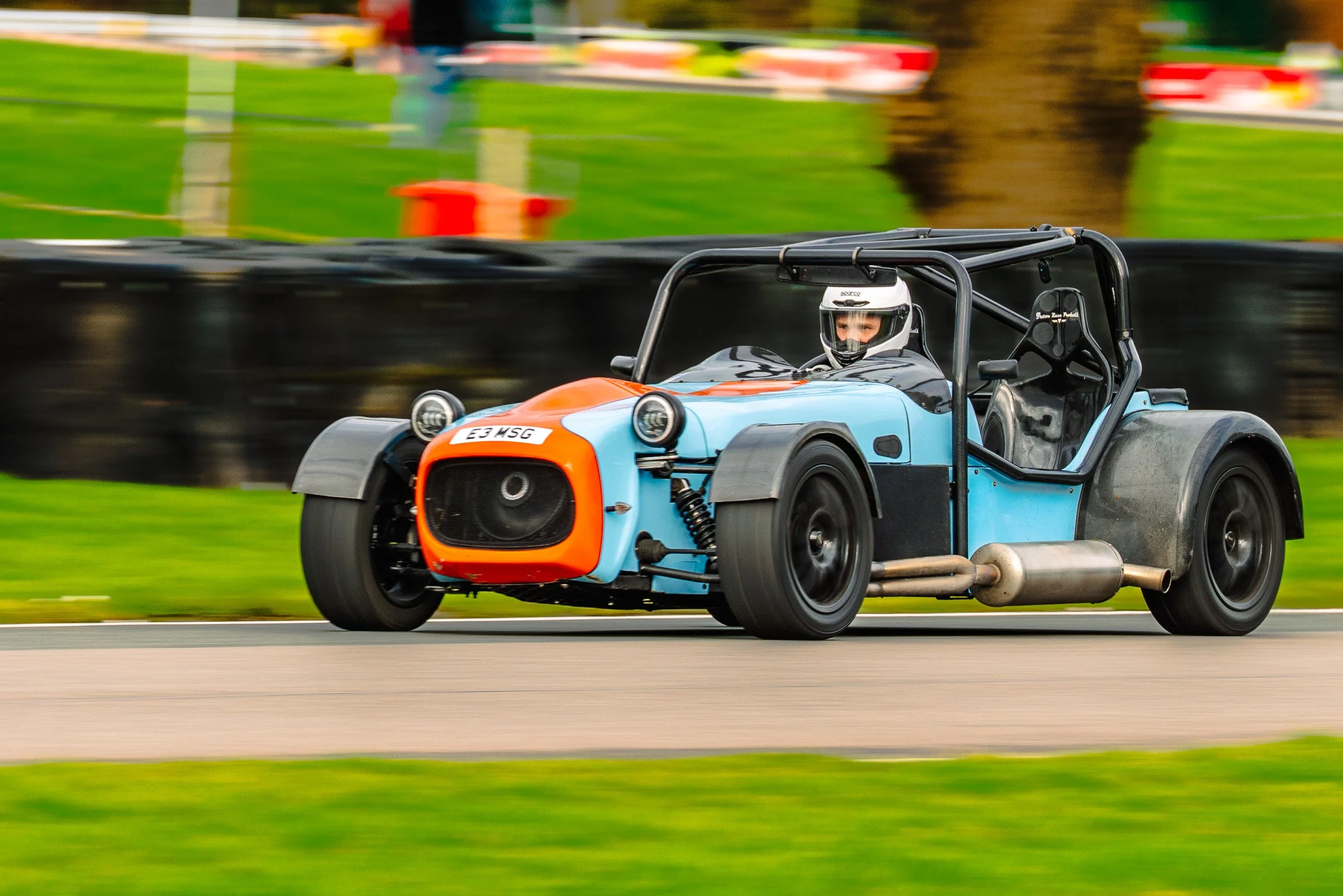 A blue and orange race car with a driver wearing a white helmet racing on a track.